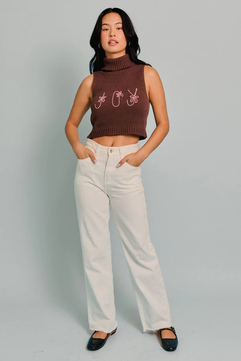 Woman in a brown turtle neck sleeveless cropped Joy Top with white pants