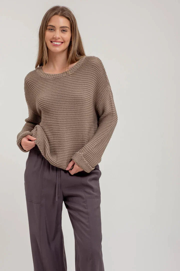 Smiling woman in a brown chunky knit pullover sweater and gray pants, showcasing boho style