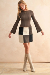 Woman wearing a ribbed long sleeve knitted top, patchwork skirt, and knee-high boots
