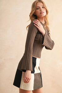 Woman modeling a brown ribbed long sleeve knitted bell-sleeve top with a color-block mini skirt