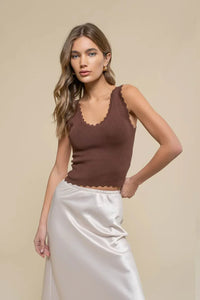 Woman in brown scallop edge sleeveless crop top and white skirt on neutral background