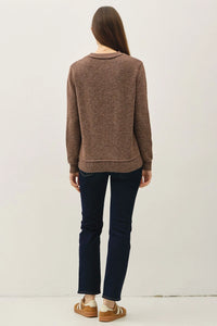 Woman wearing brown crew neck pullover with exposed seams and dark blue jeans