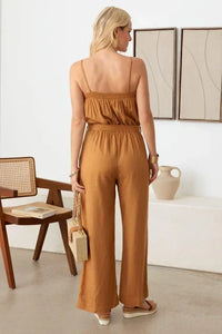 Woman in caramel sleeveless jumpsuit with flowy wide-leg pants and smocked neck line