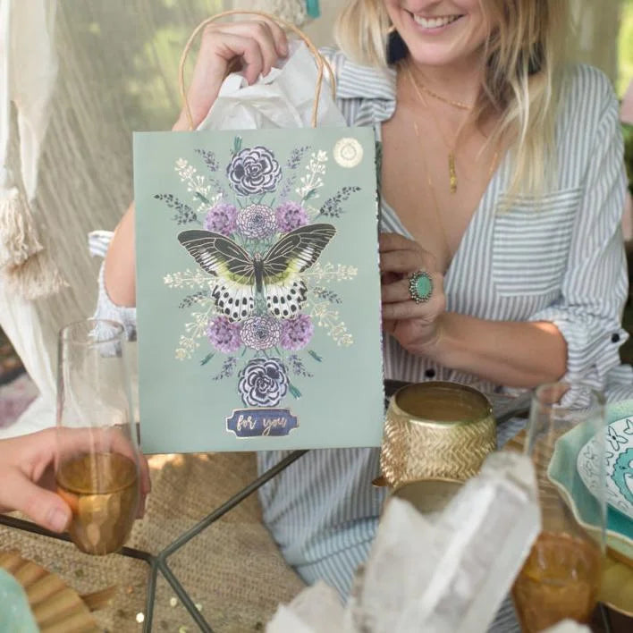 A woman presenting a card with a butterfly in a Daisy Lane gift bag