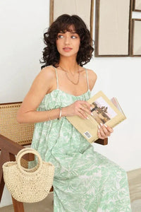 Woman in a Sleeveless Shirring Tropical Print Maxi Dress seated with a book