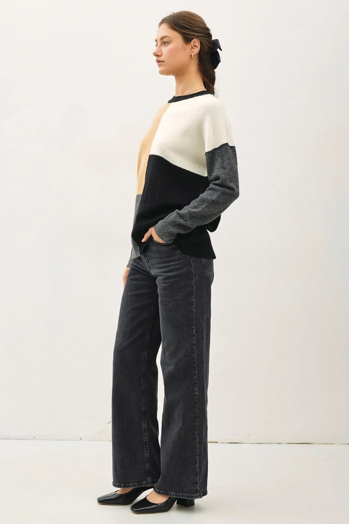 Woman in a crew neck color blocked sweater and wide-leg trousers, casually posing