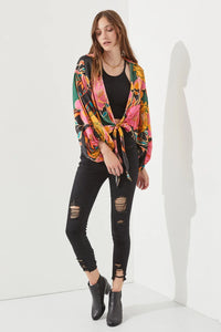 Woman in colorful jacket and jeans showcasing floral print tie-front cardigan