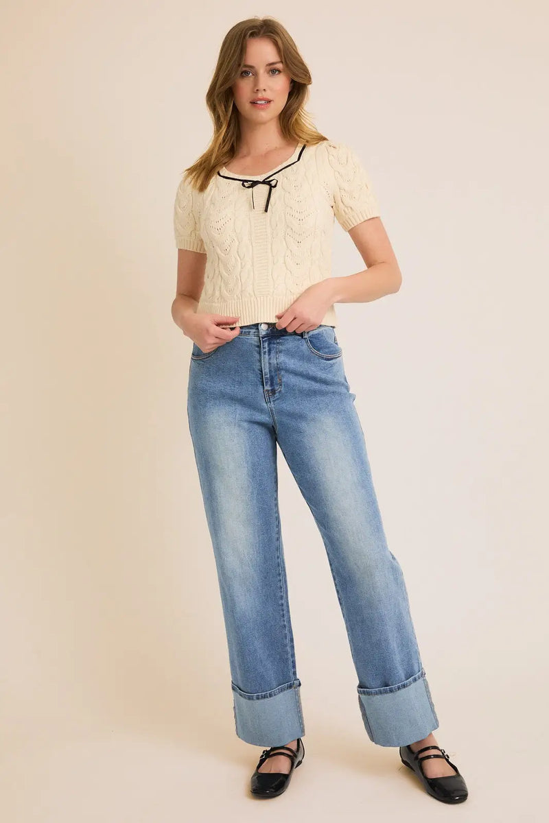 Woman in a cream square neck puff half sleeve tie cable sweater and blue jeans