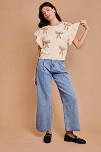 Woman in cream bow-patterned top and blue wide-leg jeans, showcasing women’s boho chic clothing