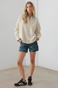 Woman in cream fleece jacket with contrast collar, denim shorts, and black sneakers