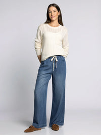 Woman wearing cream-colored knit supply Joan sweater and wide-leg blue jeans