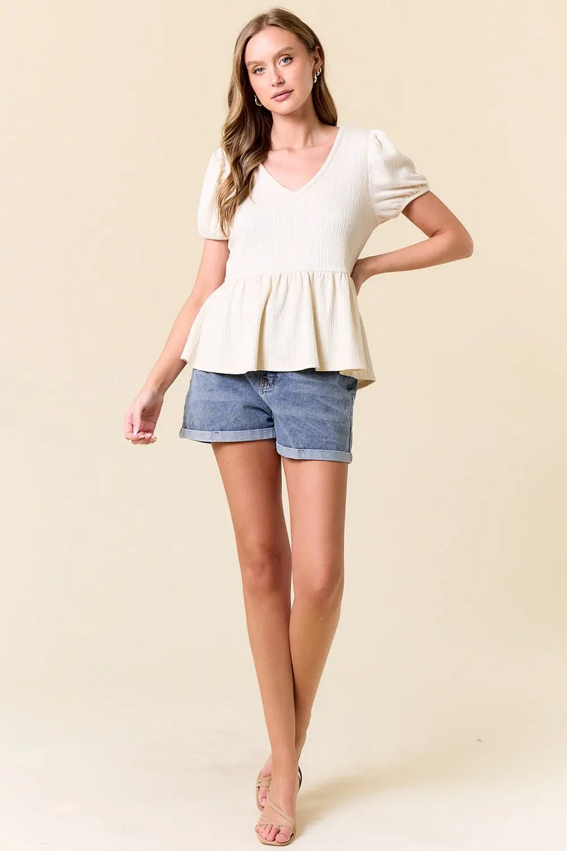 Woman in slub ribbed cream-colored peplum top and denim shorts, women’s boho chic clothing at Shop Daisy