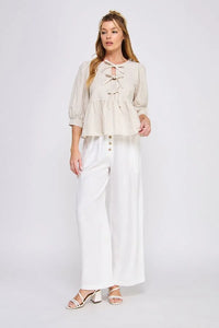 Woman in a cream puff sleeve blouse and white wide-leg pants, showcasing textured cotton blend