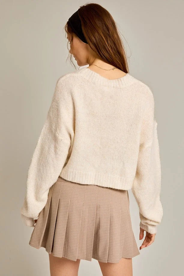 Woman in a cream ribbon crew neck sweater, paired with a beige pleated skirt