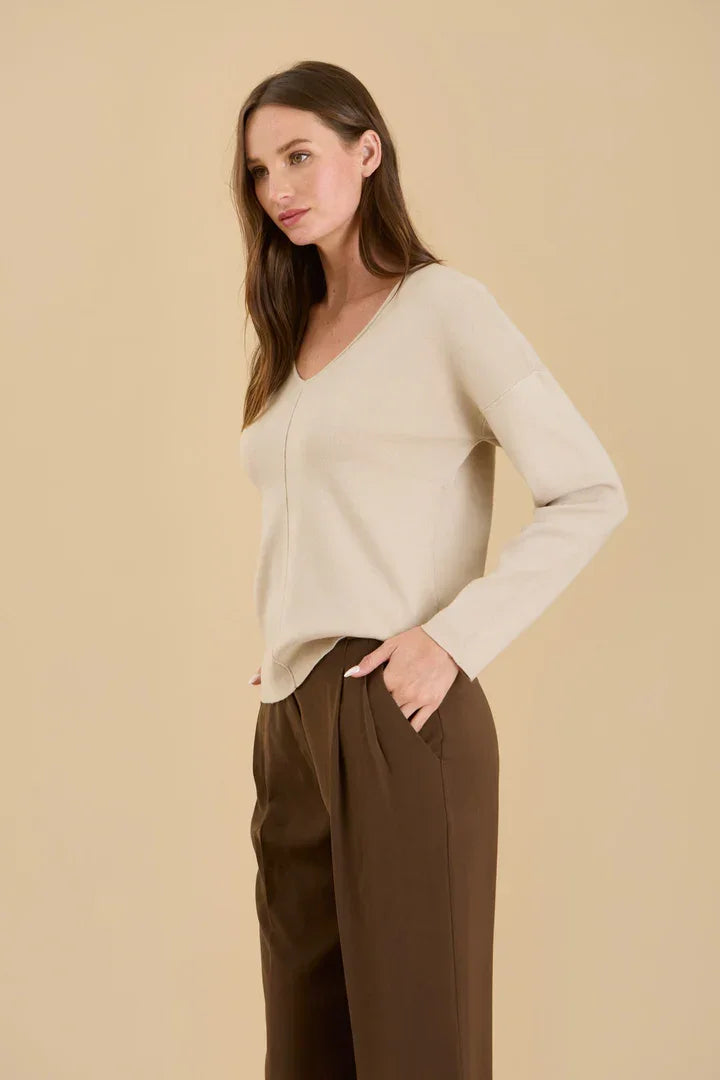 Woman wearing a cream-colored Solid V Neck Front Seam Knit Sweater and brown trousers