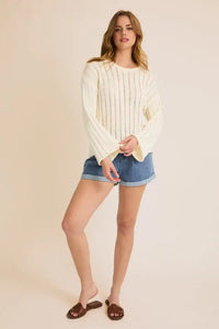 Woman wearing a cream round neck long sleeve sweater and denim shorts