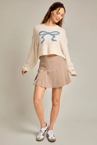 Woman showcasing a Ribbon Crew Neck Sweater Top with a bow design and pleated skirt