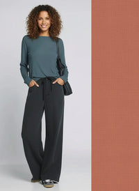Woman in teal shirt and black Austin pants holding a black shoulder bag