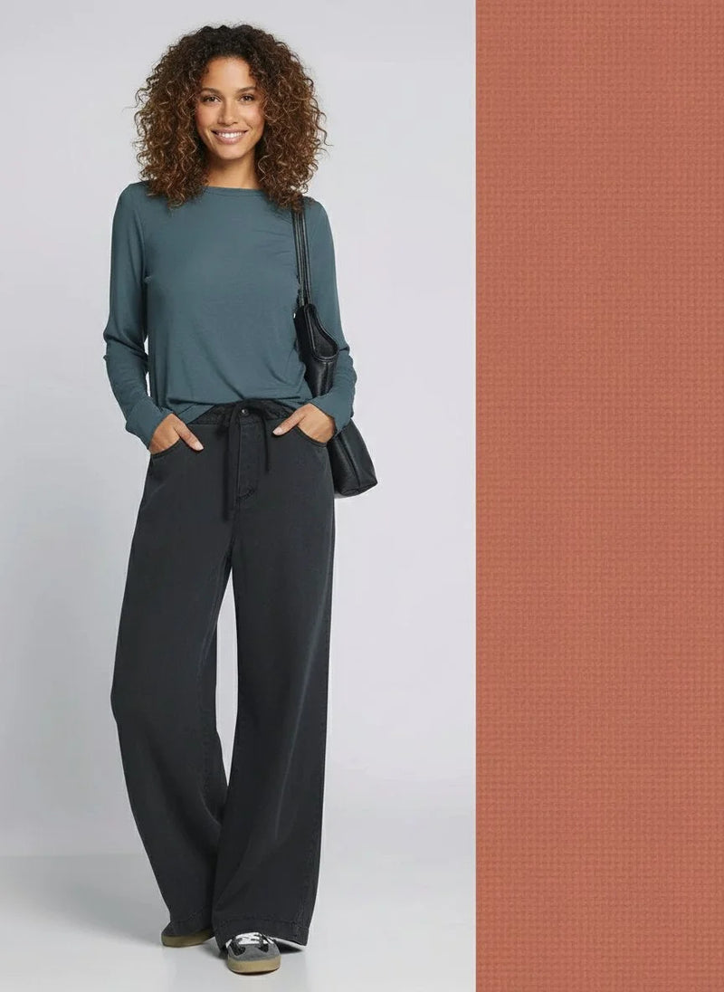 Woman in teal shirt and black Austin pants holding a black shoulder bag