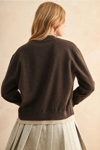 Woman wearing a dark brown long-sleeved cardigan with color contrast button details