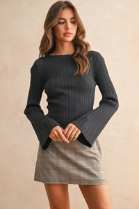 Woman wearing a dark gray ribbed long sleeve knitted top with flared cuffs and plaid mini skirt