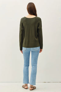 Woman in a dark green boho sweater with center seam and light blue jeans from behind