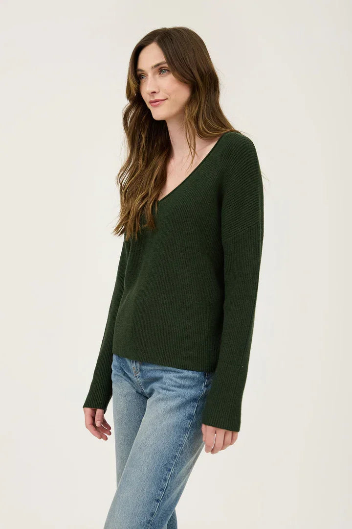 Woman in a dark green v neck long sleeve ribbed sweater and blue jeans