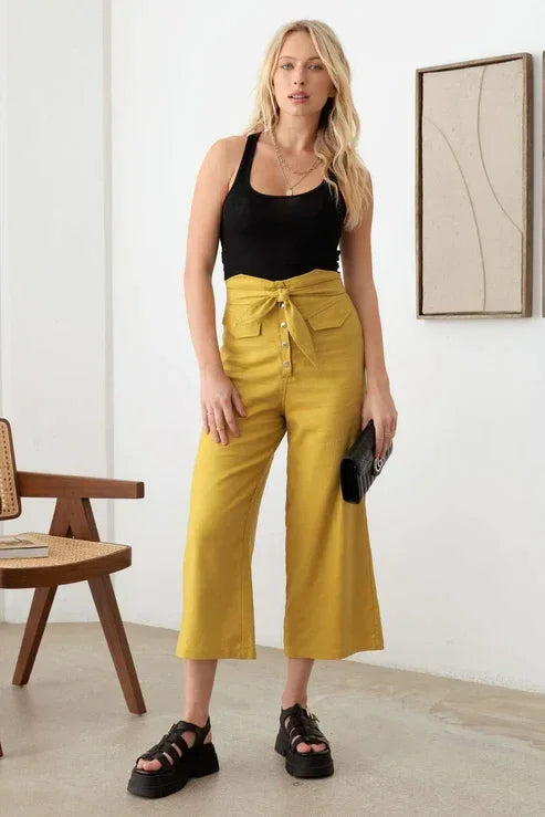 Woman in empty room showcasing belted asymmetric waistband snap button pants