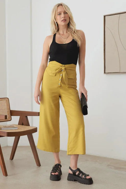 Woman showcasing BELTED ASYMMETRIC WAISTBAND SNAP BUTTON PANTS in empty room