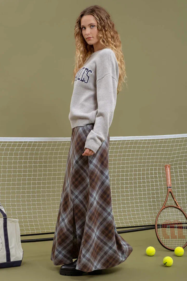 Woman in gray sweatshirt and plaid skirt on tennis court, showcasing Los Angeles Knit Crewneck