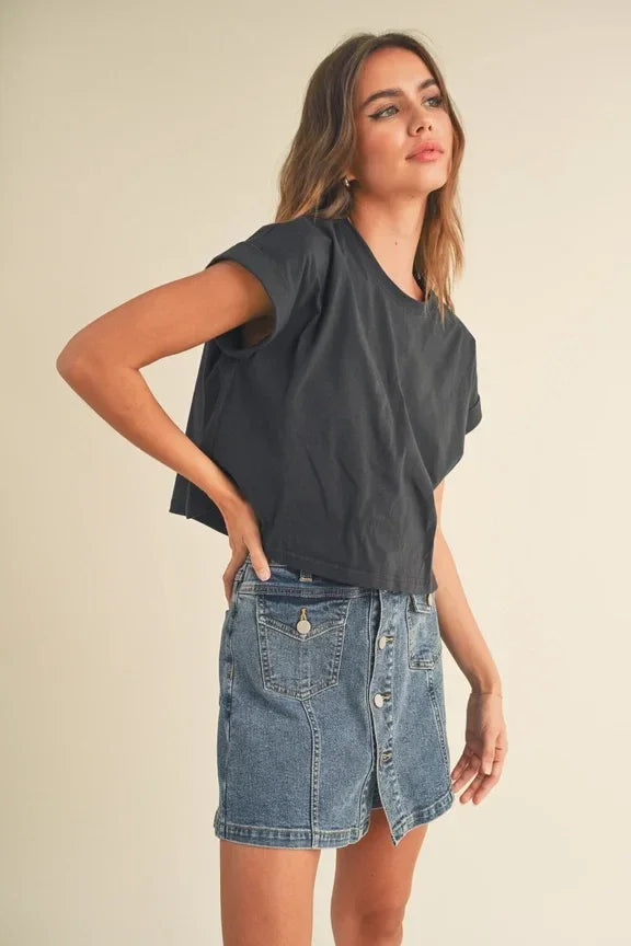 Woman in gray round neck cuffed sleeve top and denim skirt against plain background