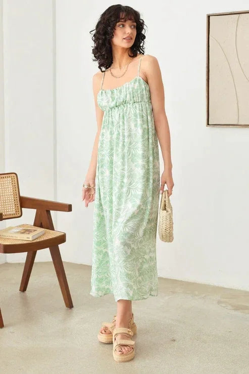 Woman in a green sleeveless shirring tropical print maxi dress in an empty room