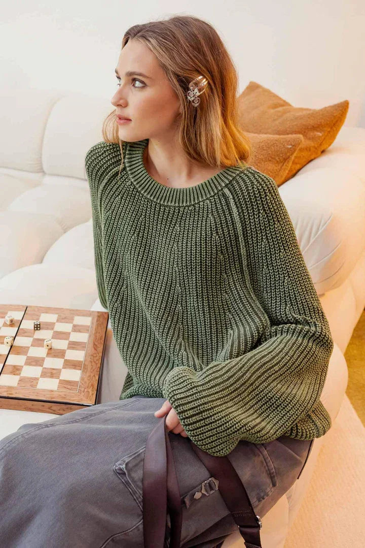 Woman in green knit pullover sweater seated beside a chess board