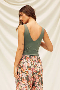 Woman in a green sleeveless top with floral pants, showcasing a double plunging bodysuit