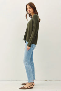 Woman in a green RELAXED V-NECK SWEATER with center seam, paired with light blue jeans