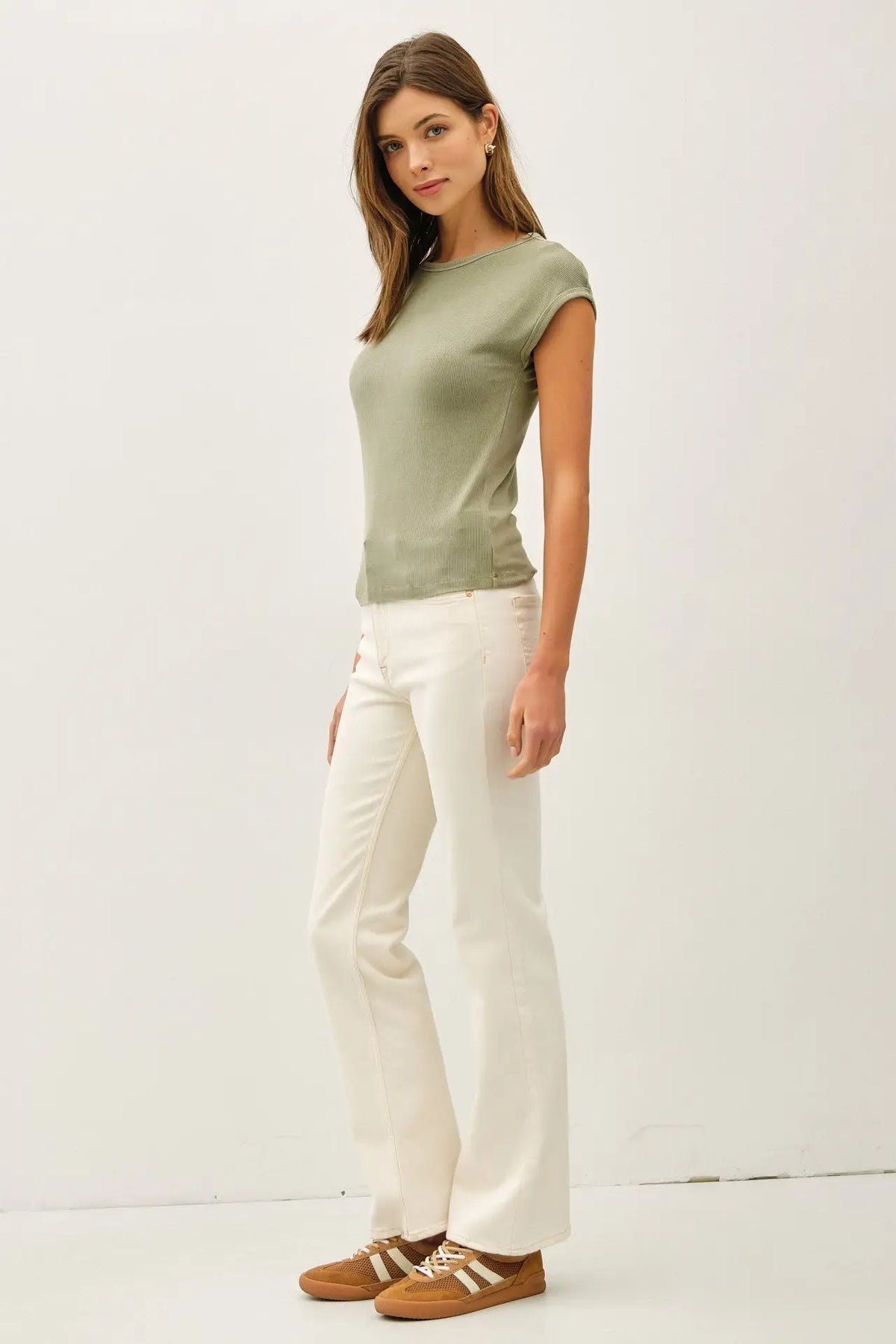 Woman wearing a green ribbed cap sleeve T shirt with white pants and brown sneakers