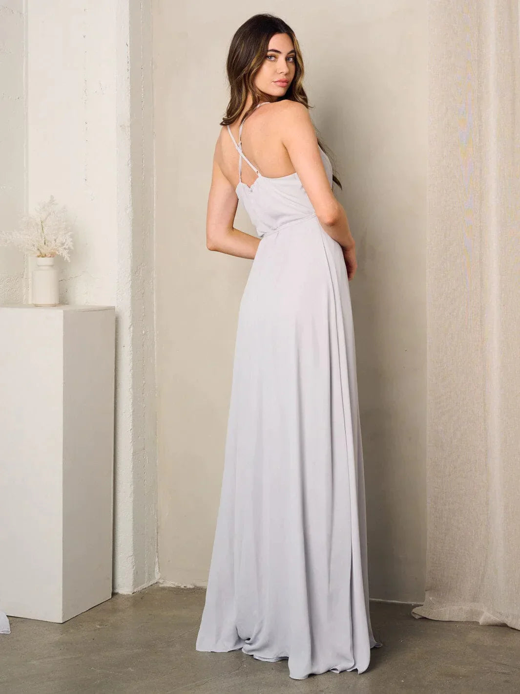 Woman in a grey sleeveless surplice tie maxi dress standing against a wall