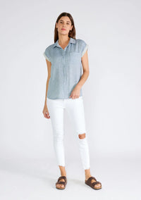 Woman in a flowy light blue Dolman Sleeve Button Front Top with white ripped jeans