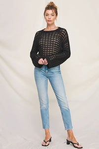 Woman in light blue jeans wearing a long flared sleeve open weave sweater with a cropped fit