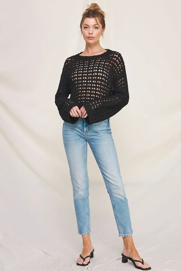 Woman in light blue jeans wearing a long flared sleeve open weave sweater with a cropped fit