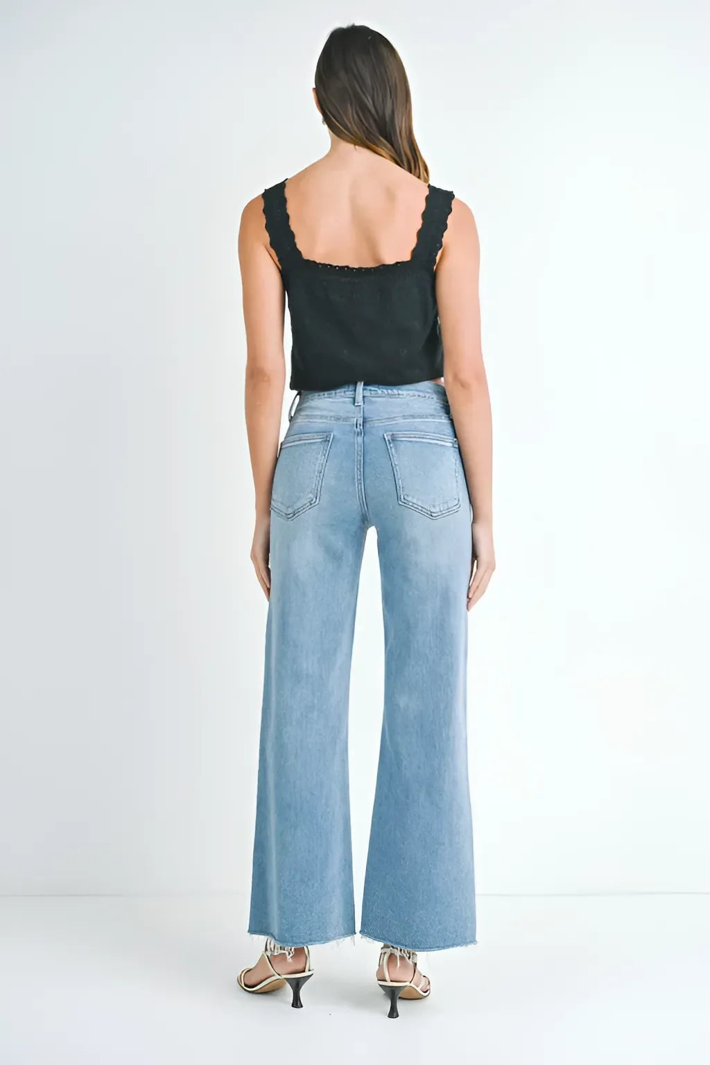 Woman in light blue long wide leg denim jeans and black sleeveless top, seen from behind