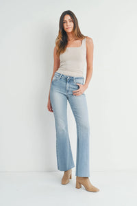 Woman in light blue mid rise flared jeans and a beige tank top for a boho look