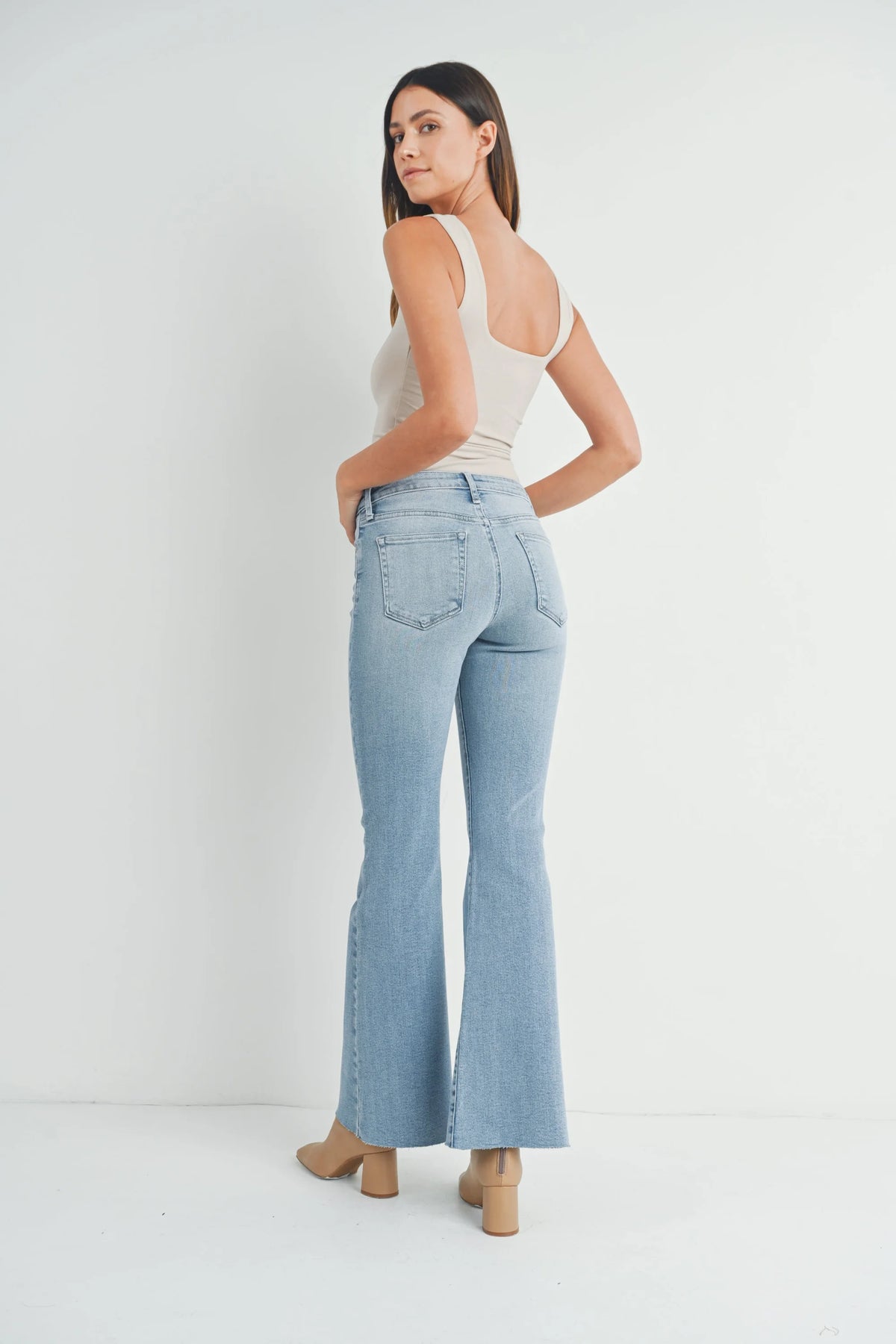 Woman in light blue mid rise flared jeans and white tank top for a boho look