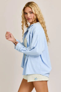 Woman in a light blue oversized shirt and shorts from Shop Daisy’s women’s boho chic clothing