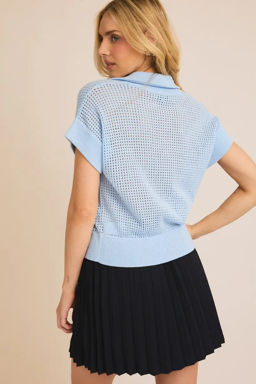 Woman in a light blue short-sleeved knit top and black pleated skirt from Shop Daisy