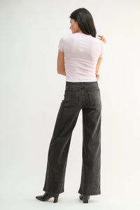 Woman wearing light purple top and dark gray patch pocket wide jeans with black heeled boots