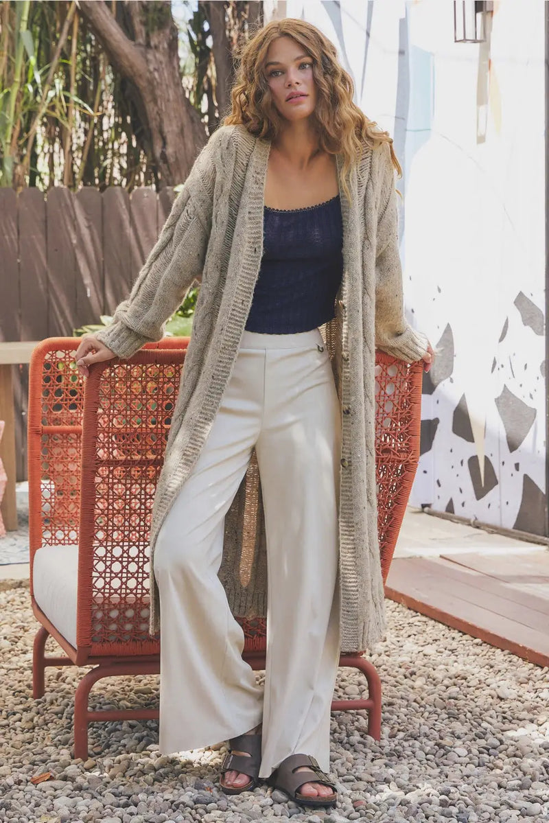 Woman wearing a long cable-knit cardigan with off-white suede wide leg pants