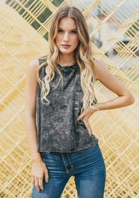 Woman with long wavy blonde hair wearing a distressed dark gray cotton muscle tee and blue jeans