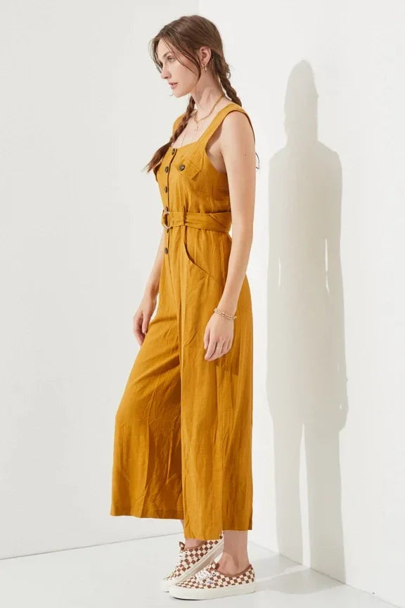 Woman in a mustard sleeveless square neck button down ankle jumpsuit