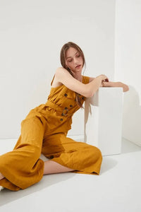 Woman wearing a stylish sleeveless square neck button down ankle jumpsuit in mustard